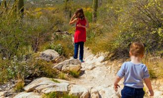 A young girl and her little brother hike down a rocky trail looking over Tucson, Arizona.